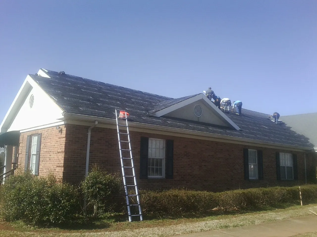 Crew tearing shingles off a brick ranch roof with a ladder set — Metal Roof Repair work by our crew in Seekonk