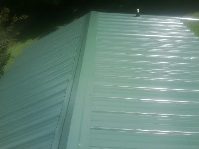 New green metal panels meeting at the ridge of a roof — Flat Roof Repair work by our crew in Seekonk