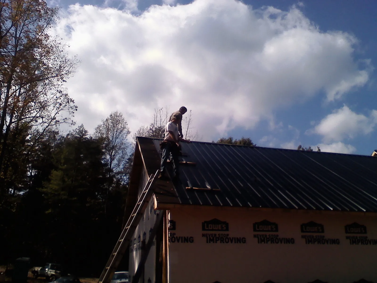 Roofer fastening dark metal panels high against a cloudy sky, from a Roof Inspection job in Seekonk