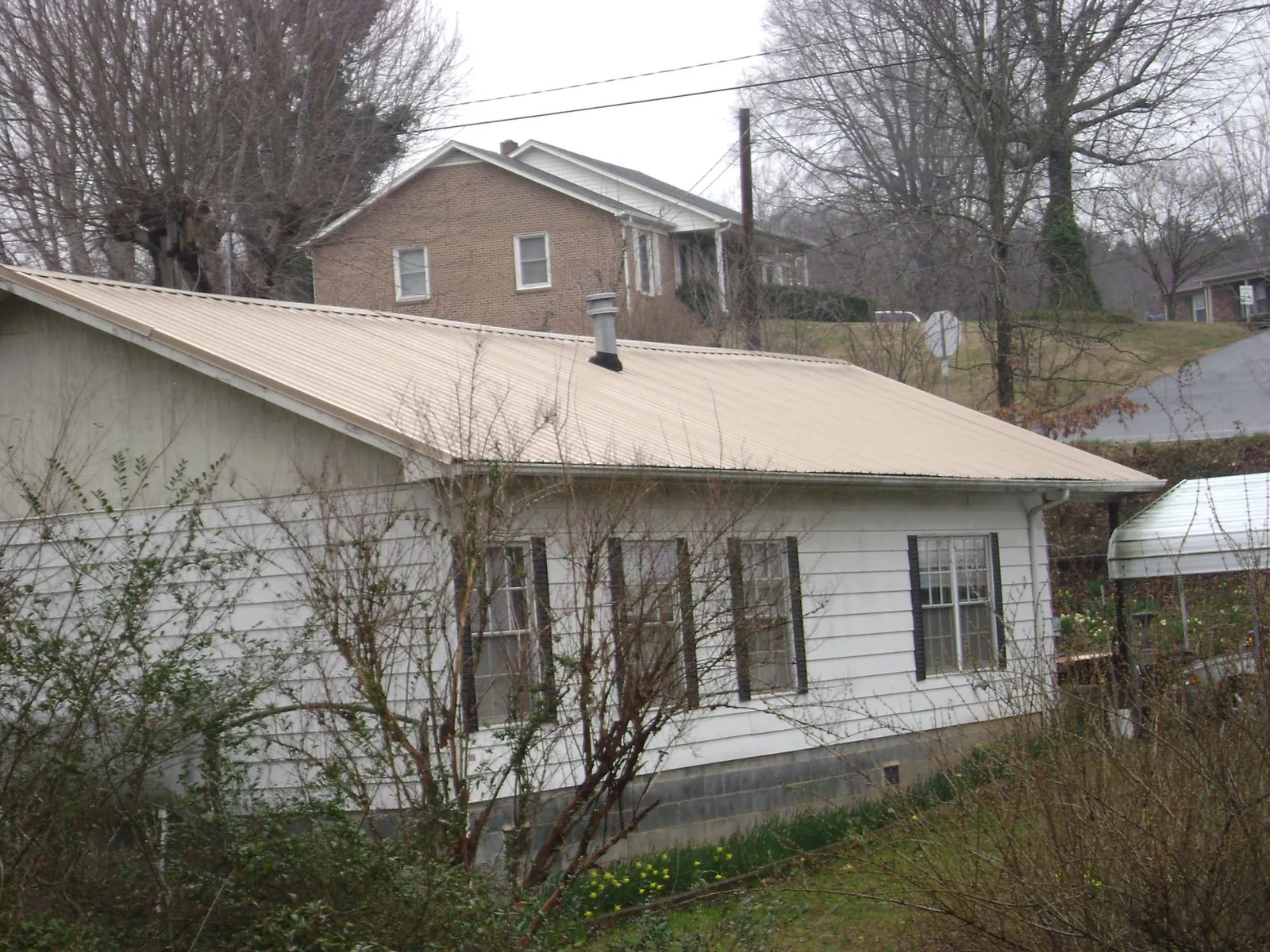 Tan metal roof on a white sided house set into a hillside — Commercial Roofing by Roofing Brothers in Seekonk